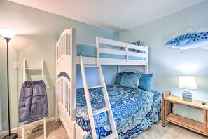 A bunk bed with a ladder, a bedside table with a lamp, and a wall decoration.