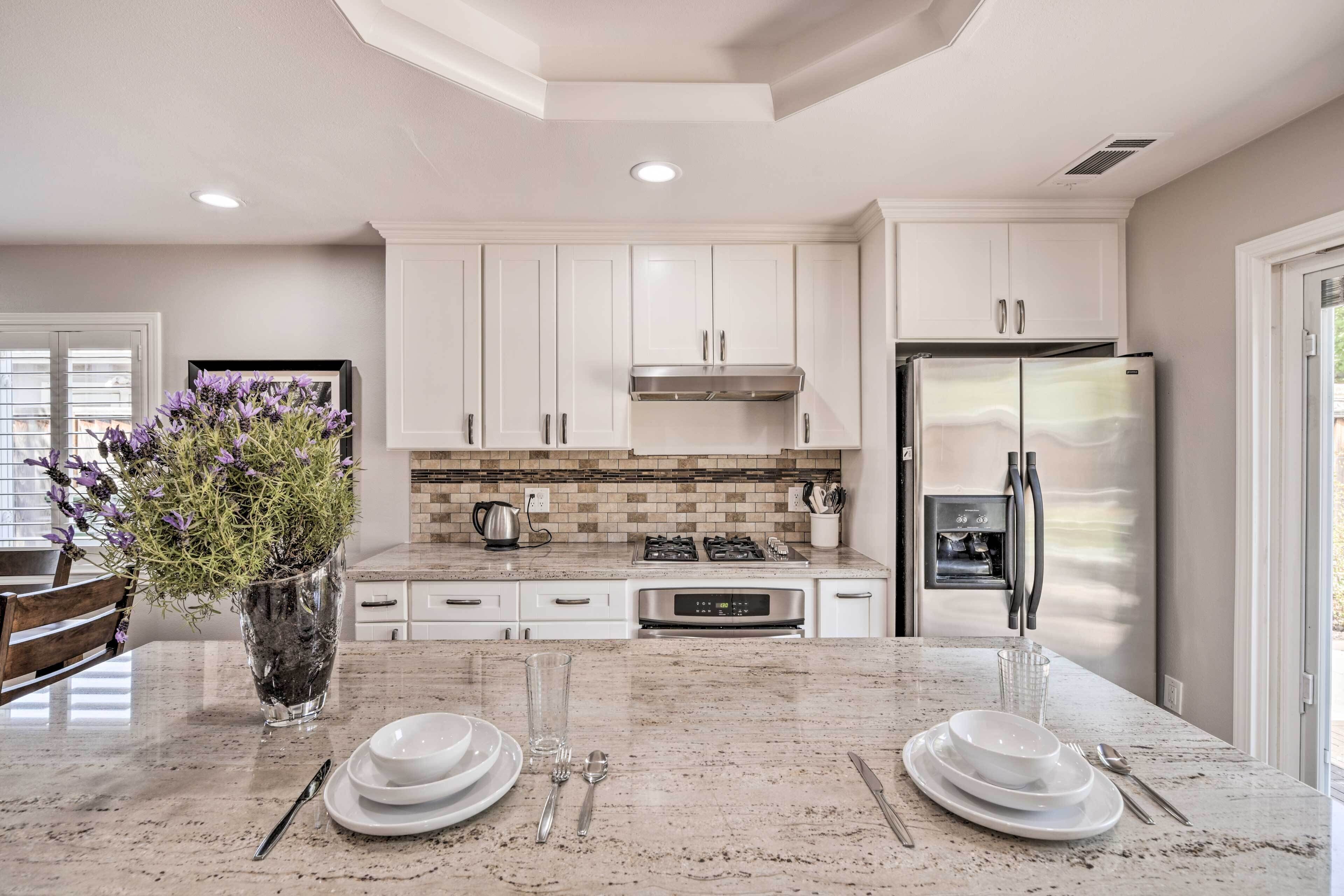 A modern kitchen with white cabinets, a stainless steel refrigerator, and a granite countertop.