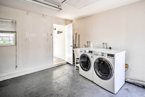 A laundry room with two front-loading washing machines, a door leading to another room, and a concrete floor.