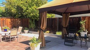 An outdoor patio area with a covered seating area, a barbecue grill, and potted plants.