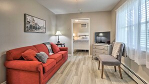 A compact living space with a red sofa, a small table, a chair, a TV, and a window with sheer curtains. - Centrally Located South Hill Apartment w/ Smart TV (Spokane)