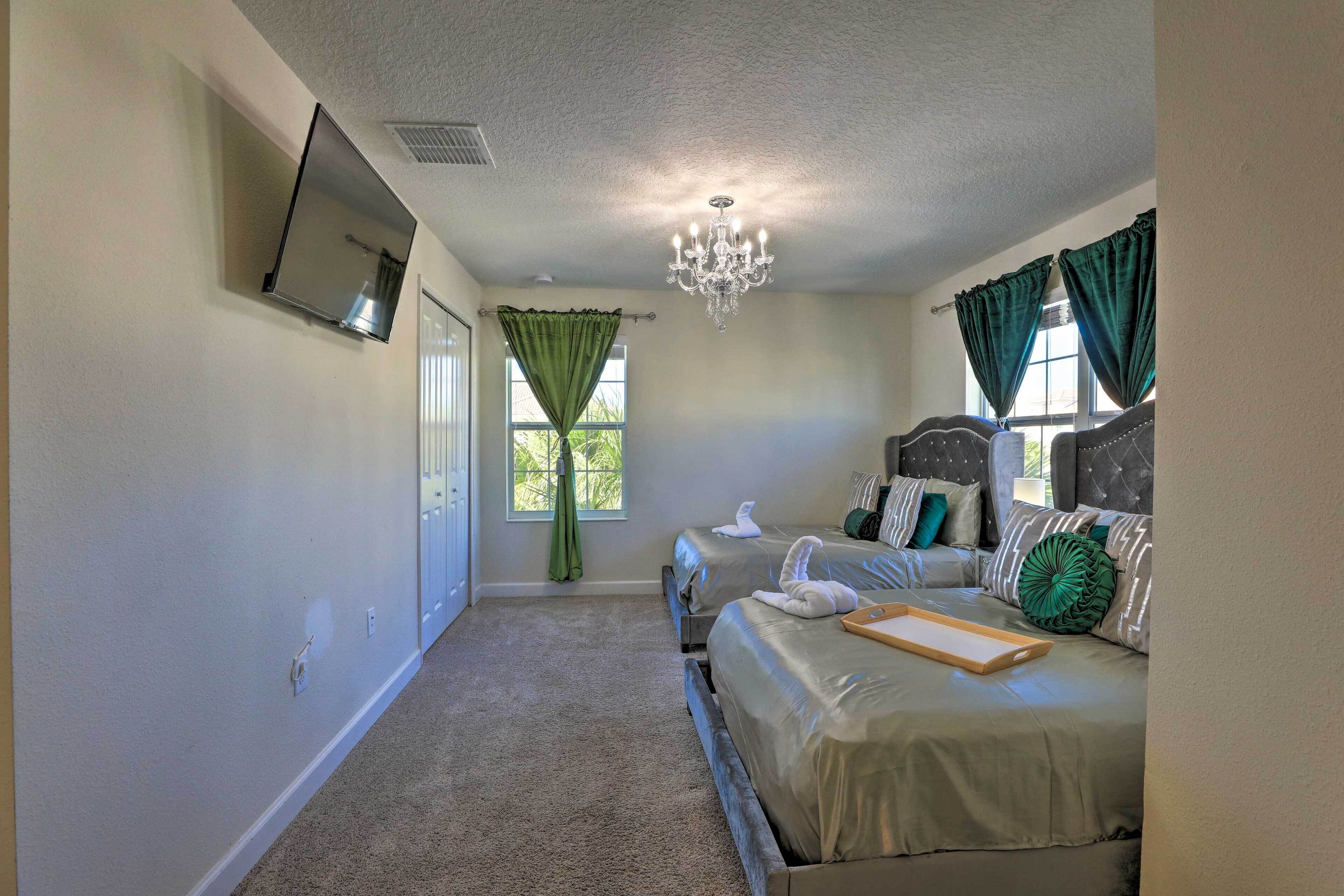A bedroom with a bed, a chandelier, a television, and a window with curtains.