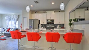 A modern kitchen with white cabinets, a stainless steel refrigerator, and a microwave. There are two red bar stools at the island. - 9 Mi to Disney: Davenport Resort Home w/ Pool (Davenport)