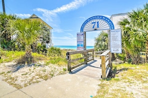 A beach entrance with a wooden boardwalk leading to a sign for Panama City Beach Public Beaches.