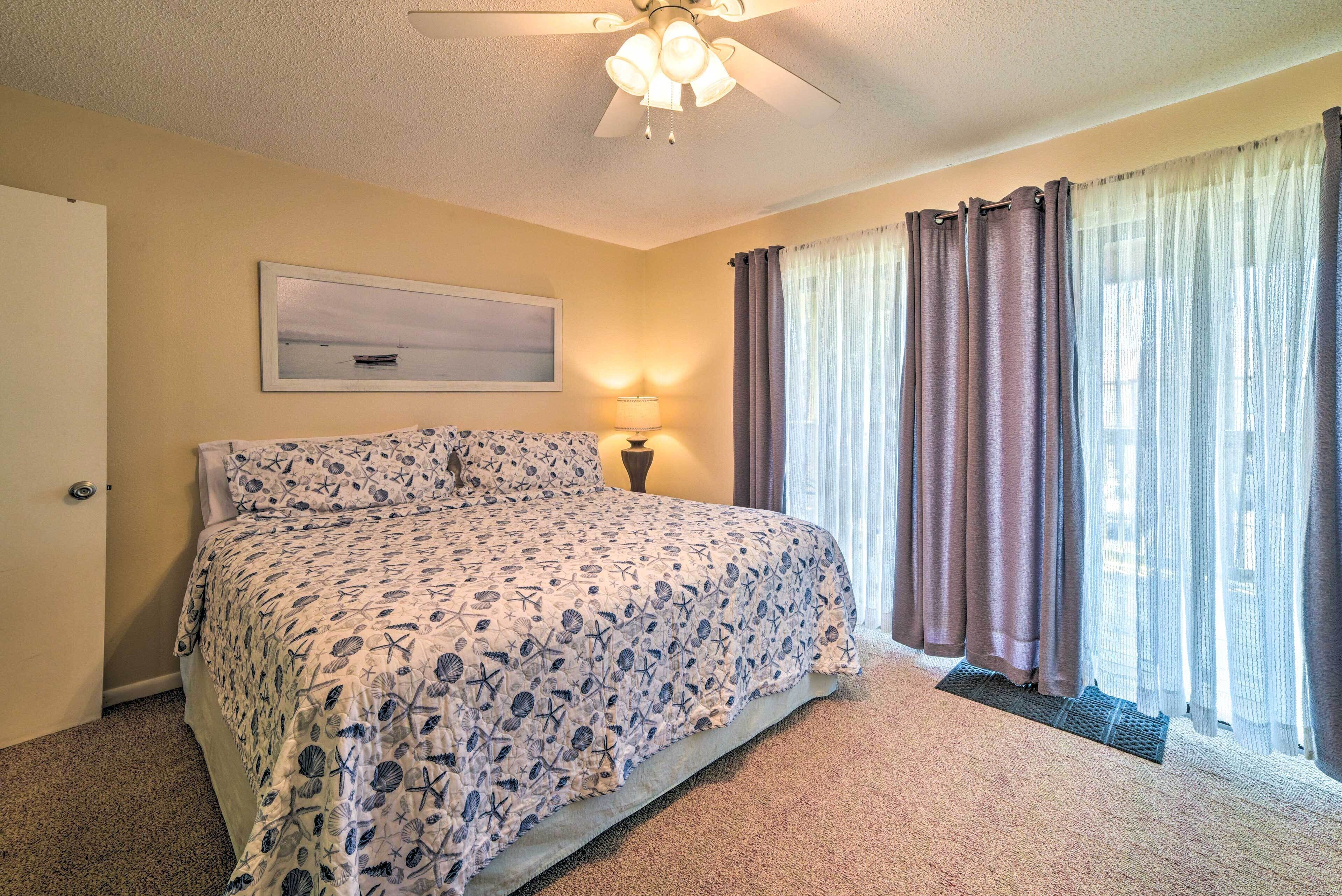 A bedroom with a bed, a ceiling fan, a window with curtains, and a wall-mounted lamp.