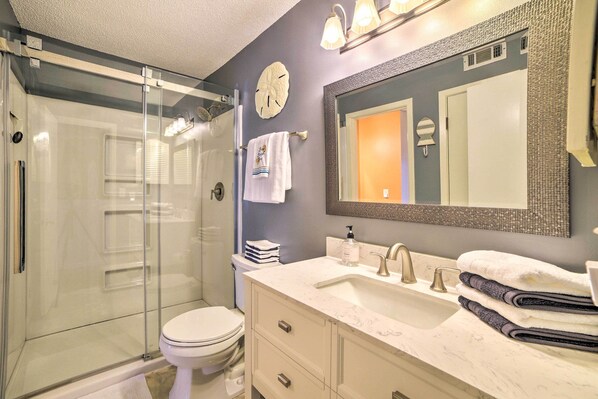 A bathroom with a glass shower enclosure, a white toilet, a vanity with a sink, and a large mirror. - Beautiful PCB Townhome: Balcony & Resort Amenities (Panama City Beach)
