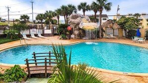 Une piscine dotée d’une terrasse en bois, de palmiers et d’une cascade décorative.