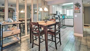 Une cuisine moderne avec des meubles blancs, un coin repas doté d’une table et de chaises en bois, et un îlot central bien visible avec un évier.