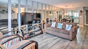 Un salon moderne avec un téléviseur à écran plat, un canapé marron, des fauteuils à rayures et une table basse en verre.