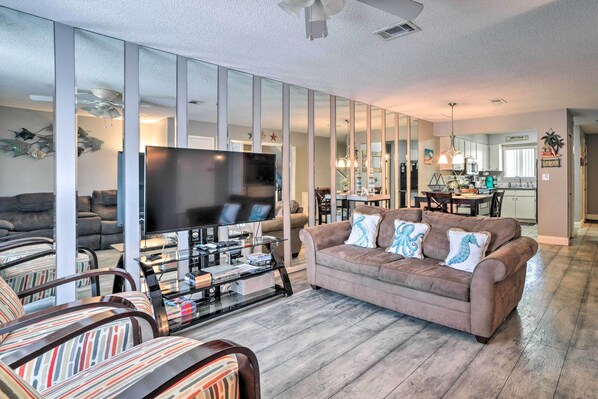 A modern living room with a flat-screen TV, a brown sofa, striped armchairs, and a glass coffee table. - Beautiful PCB Townhome: Balcony & Resort Amenities (Panama City Beach)