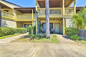 A two-story building with a balcony, a central entrance, and a small garden area with a palm tree.