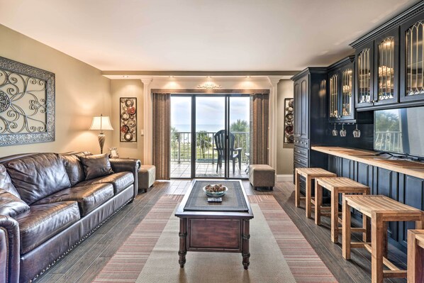 A living room with a leather sofa, a coffee table, and a kitchen area with bar stools.