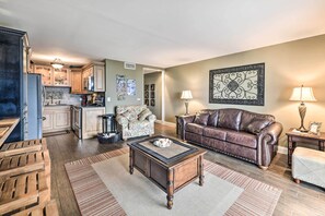 A spacious living room with a coffee table, a leather sofa, and a dining area with a kitchen in the background.