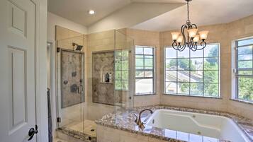 A modern bathroom with a glass-enclosed shower, a freestanding bathtub, and large windows offering a view of the outside.