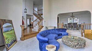 A living room with a blue sectional sofa, a round coffee table, and a painting of a vineyard. - Redding Getaway w/ Hot Tub & Outdoor Kitchen! (Redding)