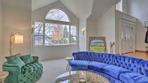 A spacious living room with a large window, a blue sectional sofa, a green tufted sofa, and a glass coffee table. - Redding Getaway w/ Hot Tub & Outdoor Kitchen! (Redding)