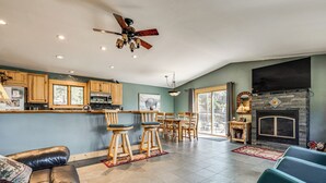 A modern kitchen with wooden cabinets, a bar area, a dining set, and a fireplace. - Estes Park Home w/ AC - 1/2 Mi to Lake & Downtown! (Estes Park)