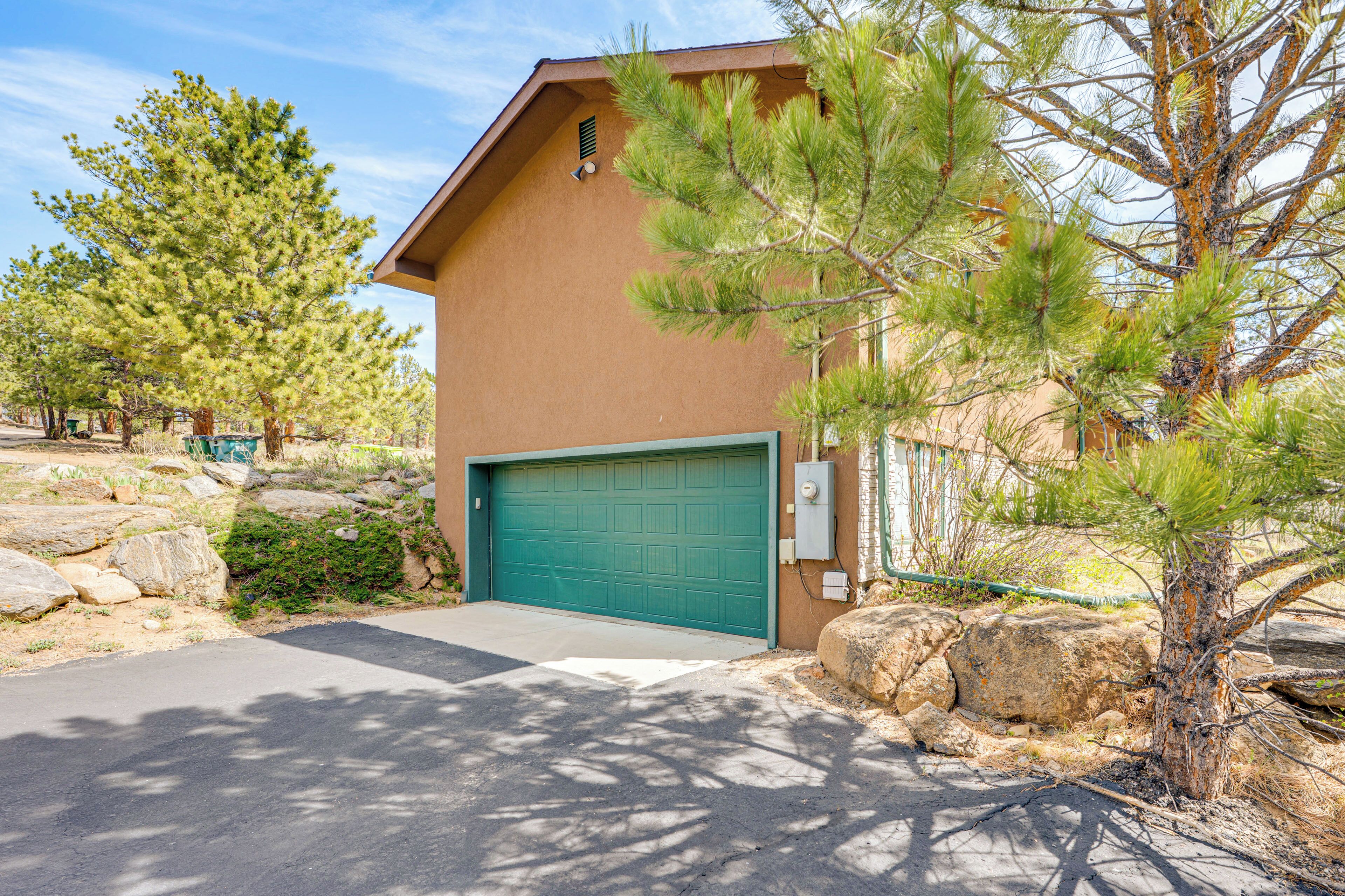 A building with a green garage door, surrounded by rocks and pine trees.