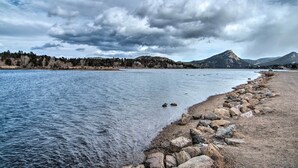 A riverside view with a rocky shoreline, trees, and distant mountains under a cloudy sky. - Estes Park Home w/ AC - 1/2 Mi to Lake & Downtown! (Estes Park)