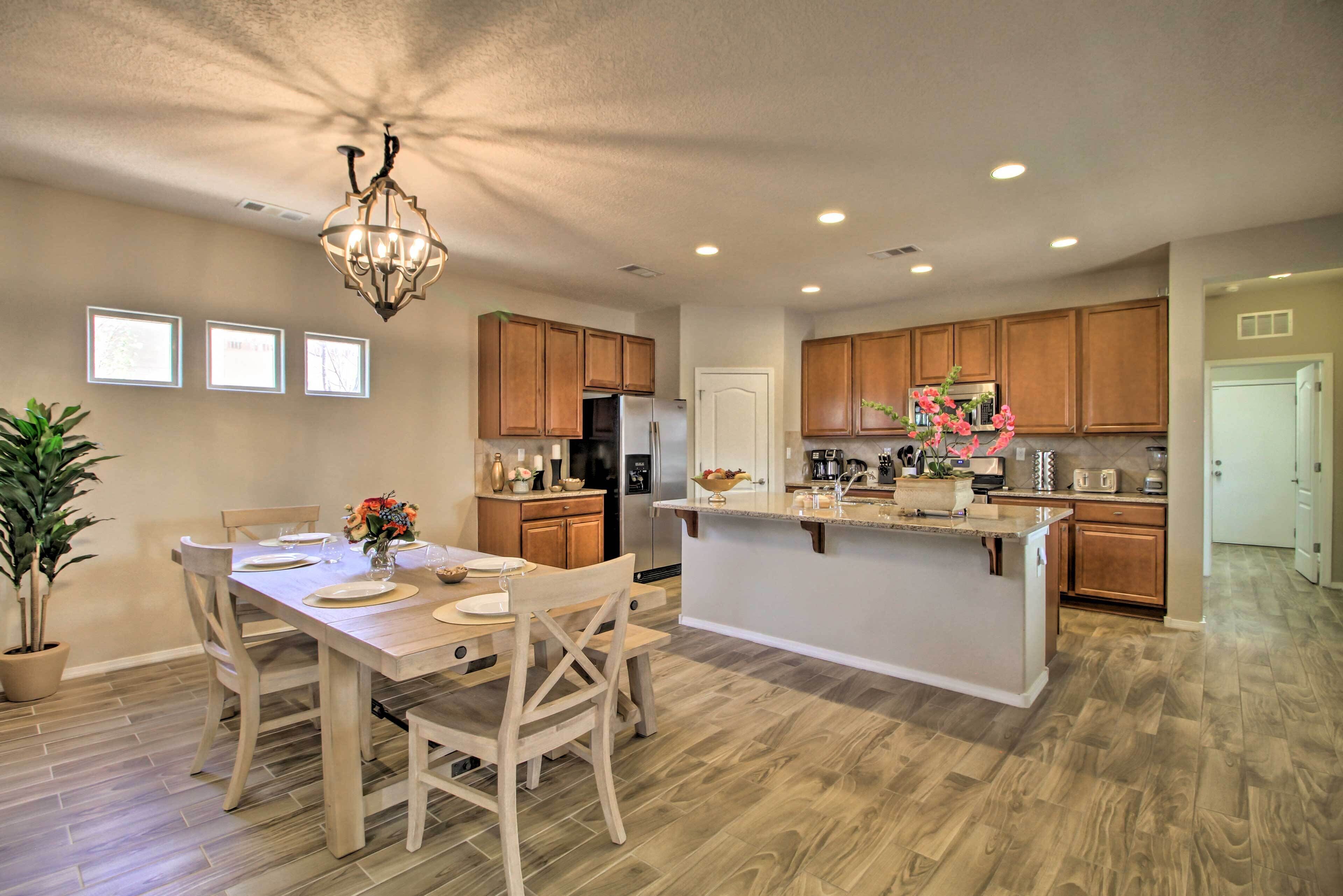 A modern kitchen with wooden cabinets, a central island, and a dining area with chairs and a table.