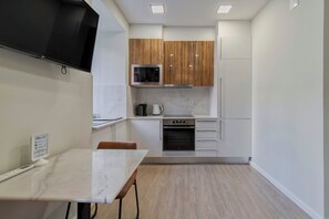 A modern kitchen with white cabinets, a microwave, a coffee maker, and an oven. There is a marble countertop and a dining table with chairs. - Canto Doce Alojamento Troino I (Setúbal)