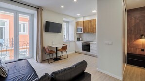 A modern apartment with a kitchenette, a dining area with a table and chairs, a sofa, and a balcony with a railing. - Canto Doce Alojamento Troino I (Setúbal)