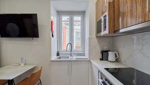 A compact kitchen with a window, a microwave, a kettle, and a stove. - Canto Doce Alojamento Troino I (Setúbal)