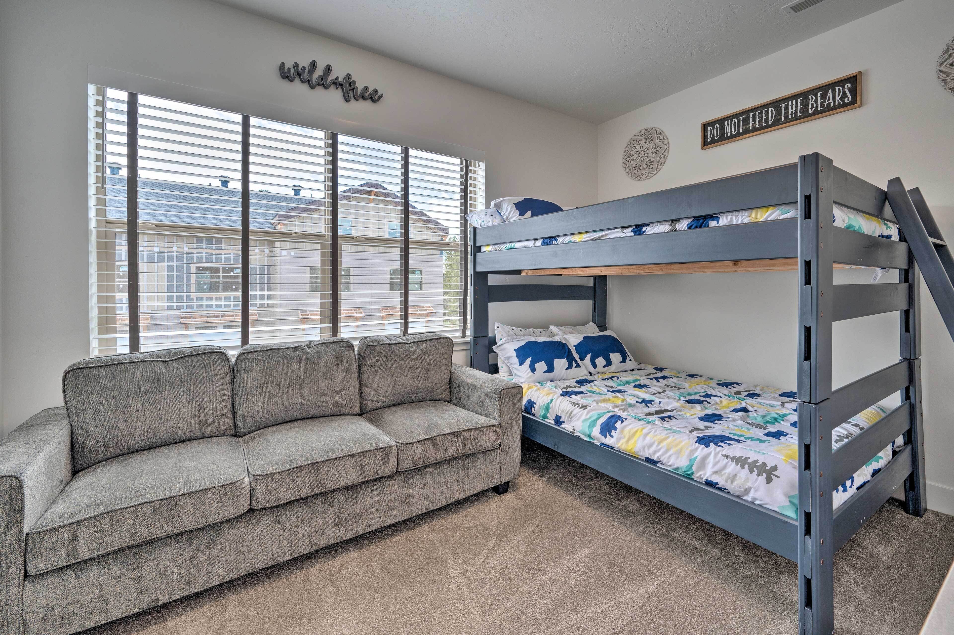 A bedroom with a bunk bed, a gray sofa, and a window with blinds.