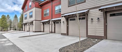 A row of townhouses with attached garages, a concrete driveway, and a landscaped area with small trees.