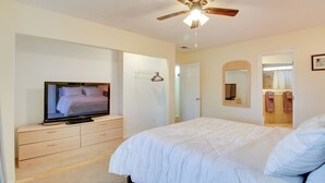 Une chambre à coucher avec un lit, un téléviseur posé sur une commode, un ventilateur de plafond et un miroir.