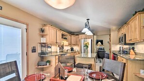 A modern kitchen with wooden cabinets, a stainless steel refrigerator, and a dining area with a wooden table set for four. - Family-friendly Home w/ Hot Tub: 1 Mi to Dtwn (Estes Park)