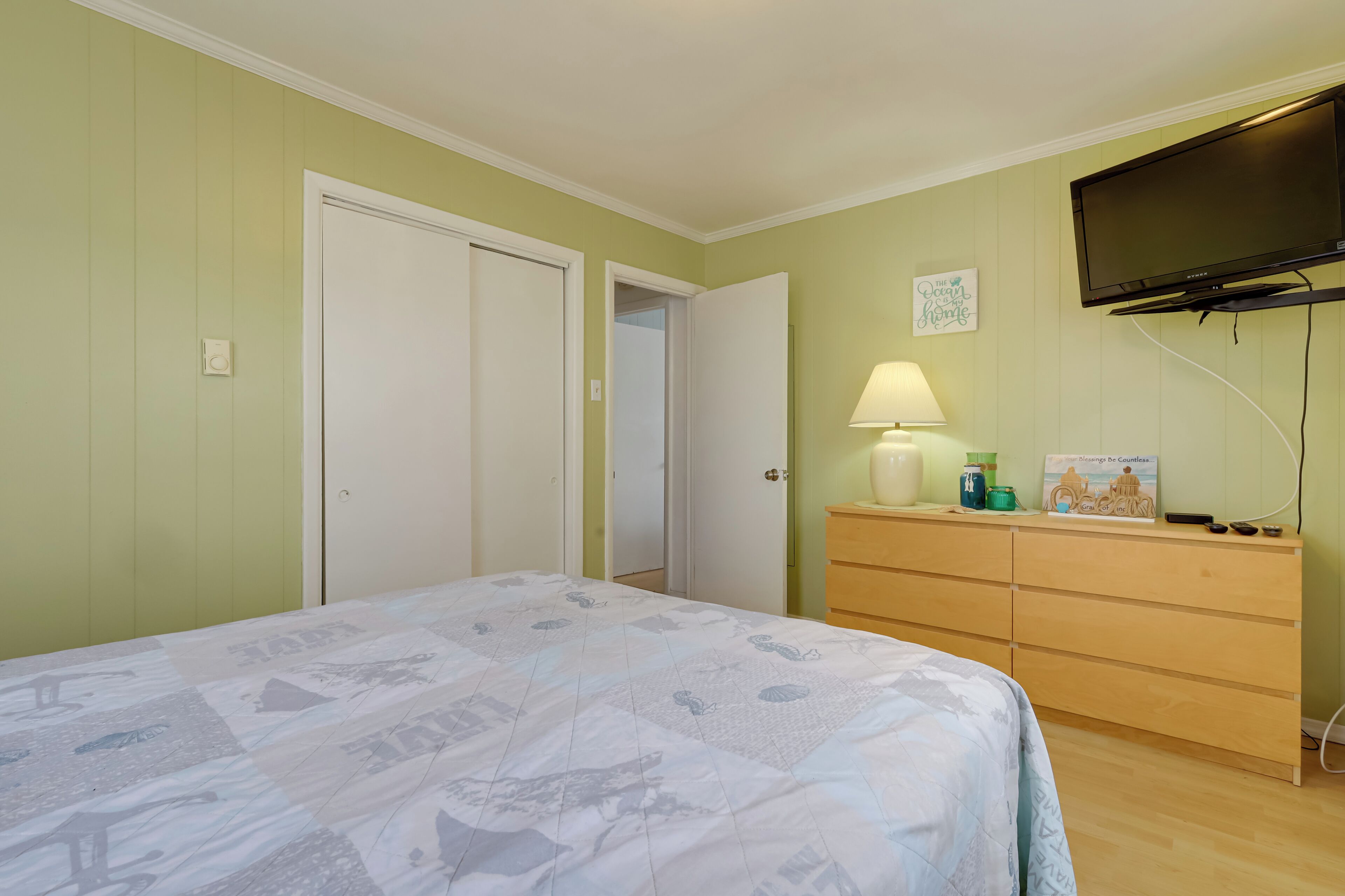 Ein Schlafzimmer mit Bett, Kommode, Fernseher und einer Tür.