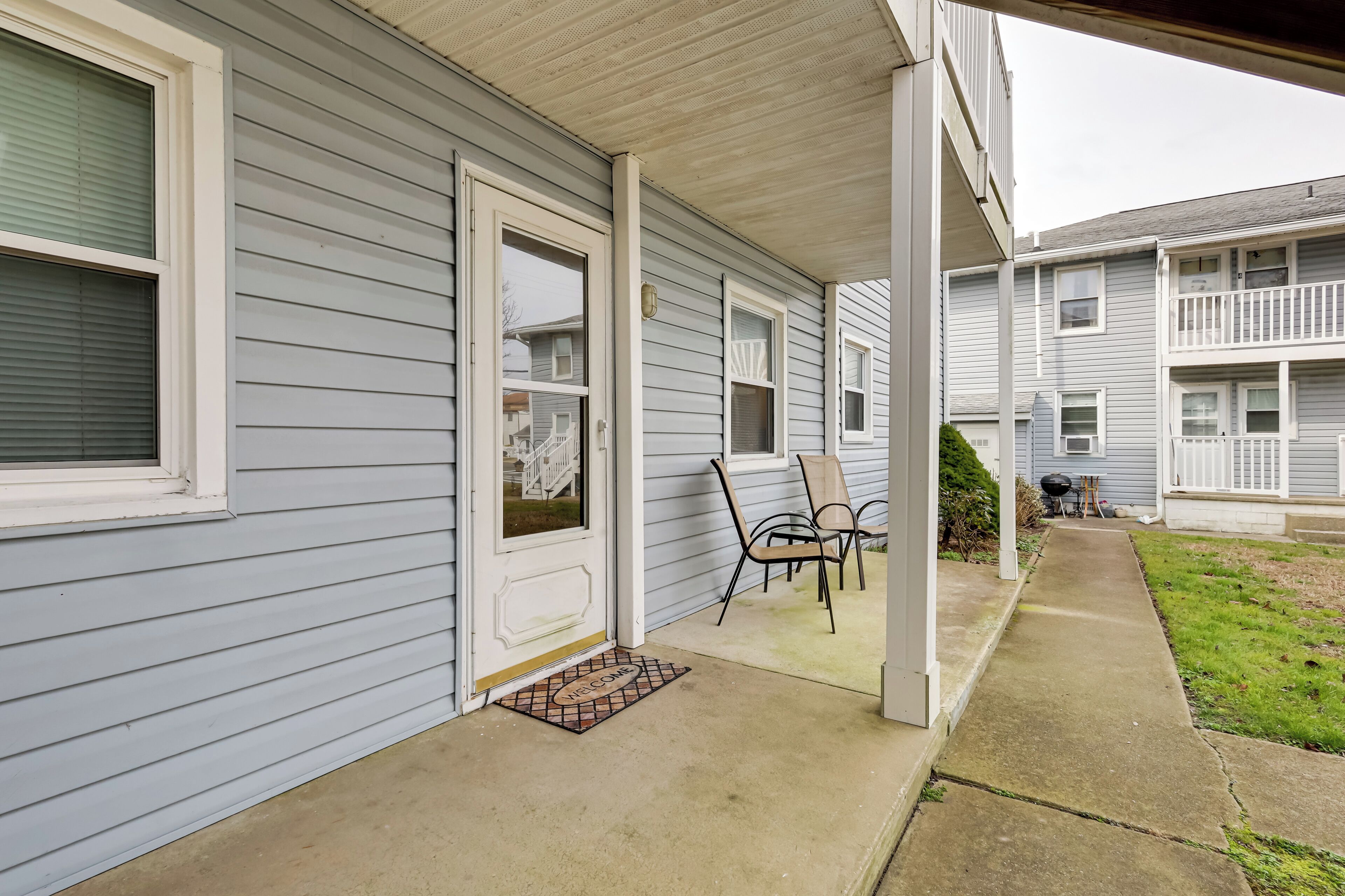 A residential building with a covered porch, a welcome mat, and a small garden area.