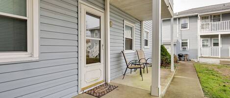 A residential building with a covered porch, a welcome mat, and a small garden area.