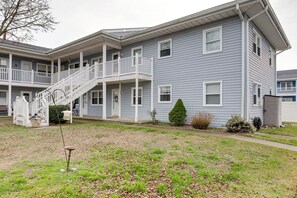 A two-story building with a balcony on the second floor, a covered front porch, and a small front yard with a bird bath and a tree. - Bay Access: 'the English Condo' in Ocean City (Ocean City)