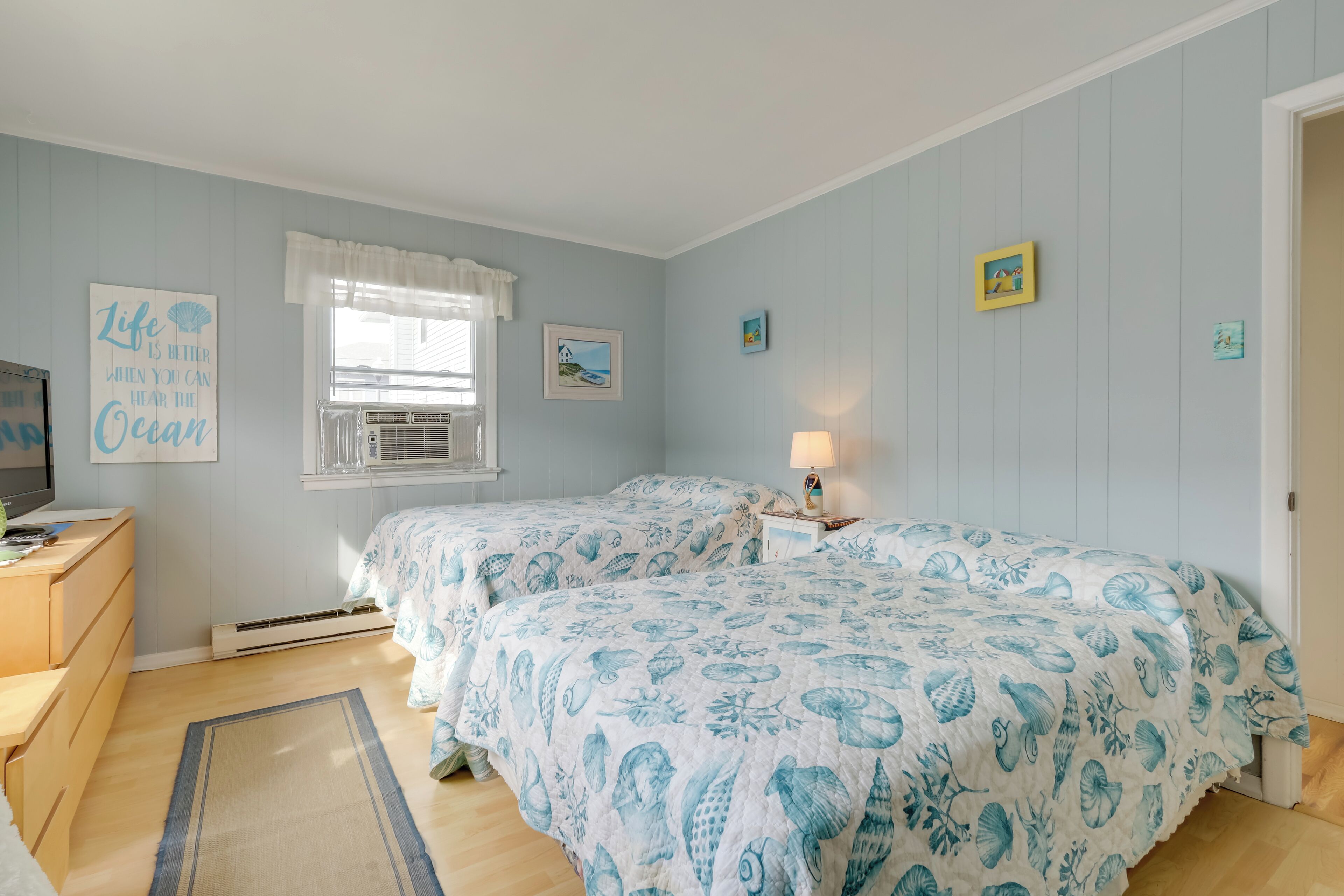 A bedroom with two beds, a dresser, a television, and a window with curtains.