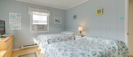 A bedroom with two beds, a dresser, a television, and a window with curtains.