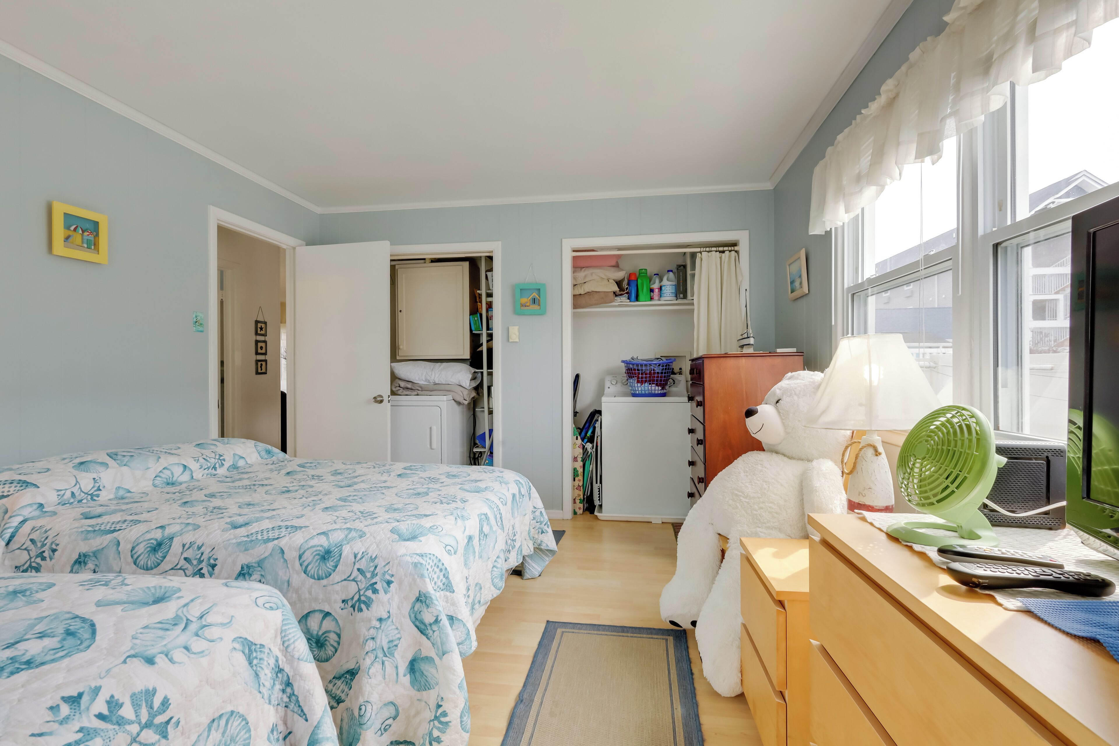 A bedroom with two beds, a desk with a computer, a fan, and a teddy bear.