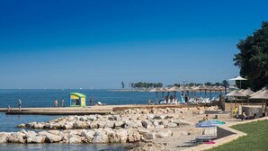 A beach with a rocky breakwater, lounge chairs, umbrellas, and a lifeguard station. - APP ELLY - 2 min from the beach! (Novigrad)