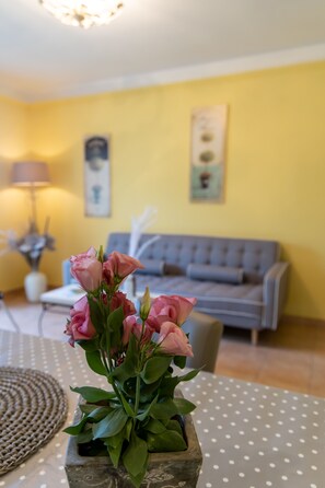 A room with a sofa, a table with a polka dot tablecloth, and a vase of pink flowers.