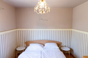 A neatly made bed with white linens, a chandelier, and a wall with the word "Dream" written on it.