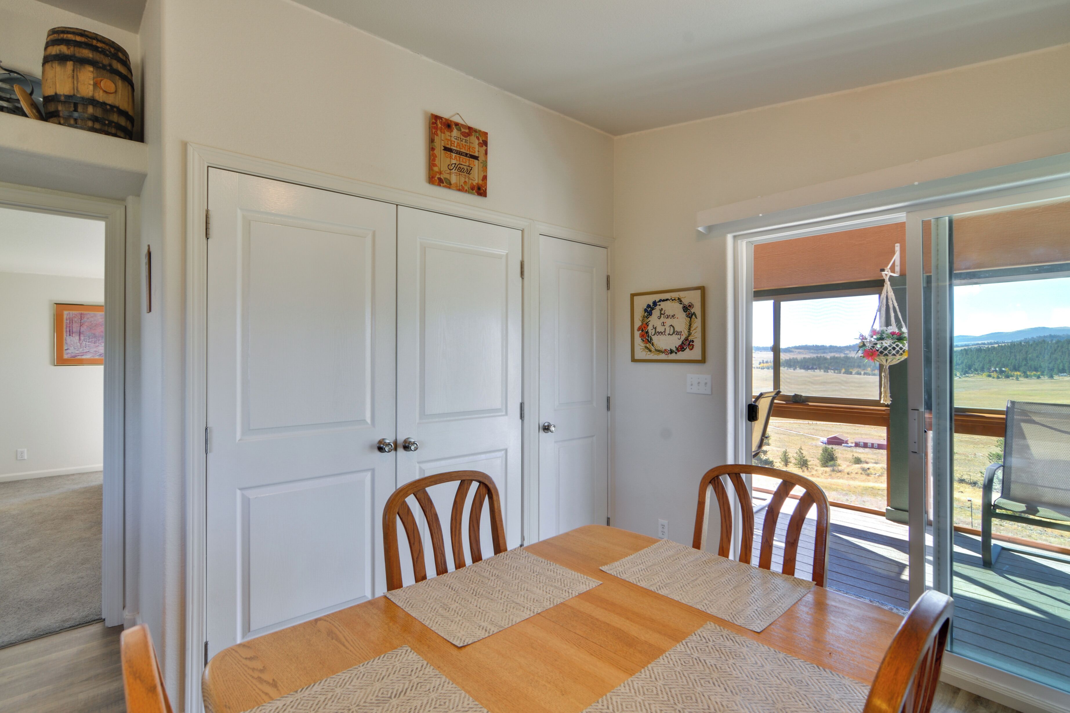A dining area with a wooden table and chairs, a white door, and a view through a glass door to an outdoor deck.
