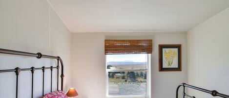 A bedroom with a bed, a window with a view of the countryside, and a framed picture on the wall.