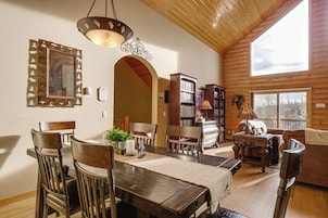 Un salón espacioso con techo de madera, una zona de comedor con mesa y sillas de madera, y una chimenea acogedora.