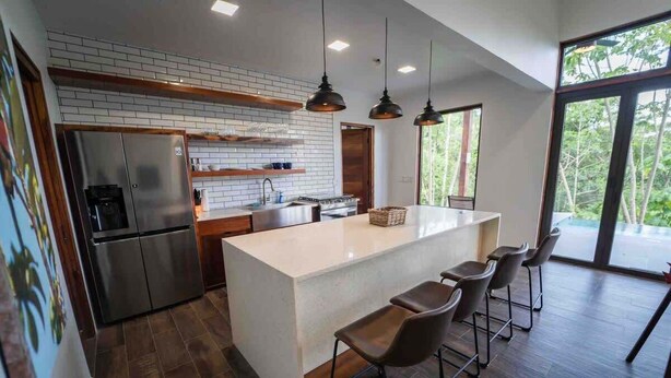Een moderne keuken met een centraal eiland, barstoelen en hanglampen.