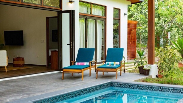 A pool area with two lounge chairs, a tiled pool, and a wooden deck.