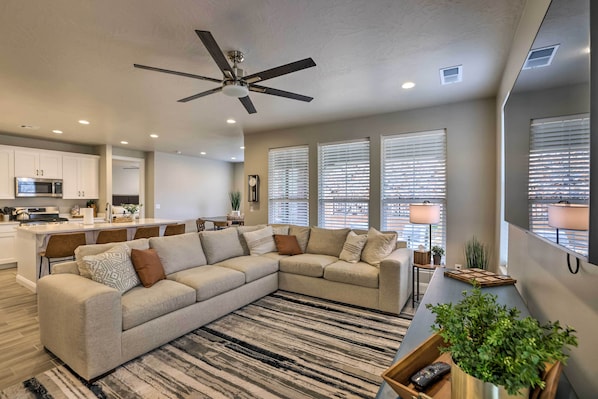 A modern living room with a sectional sofa, a ceiling fan, and a kitchen area in the background. - 37 Mi to Zion: Family Escape w/ Pool Access! (Washington)