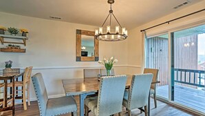 Un coin repas avec une table en bois, quatre chaises rembourrées, un lustre, un miroir et une vue sur l’extérieur grâce à une porte coulissante.