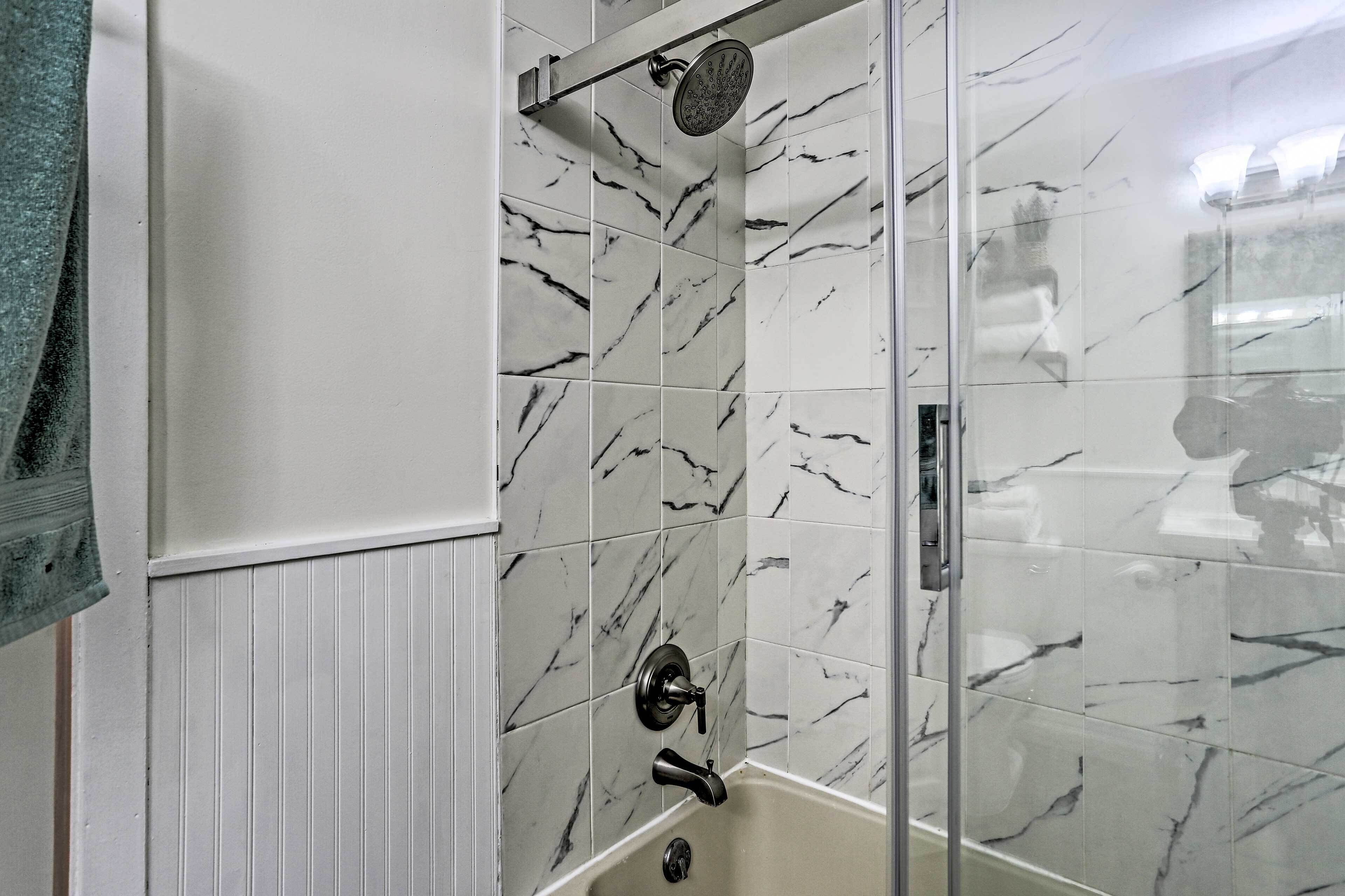 A bathroom with a glass-enclosed shower, white walls, and marble tiles.