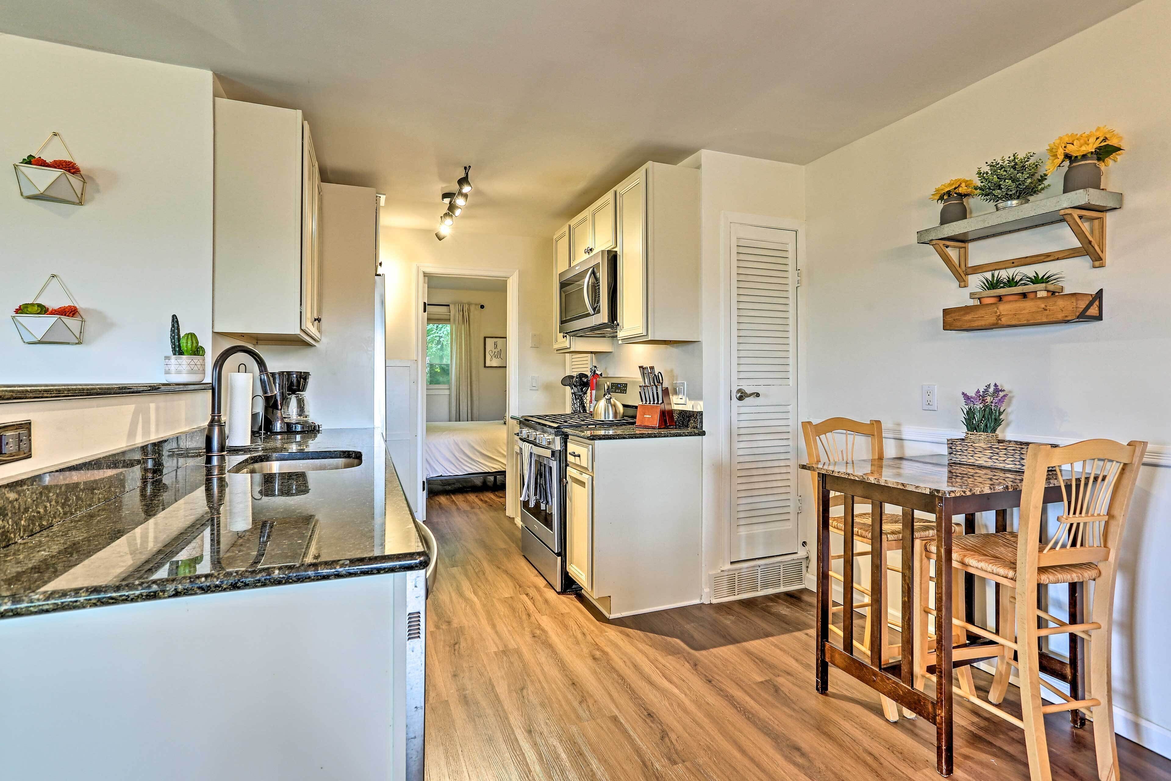 Una cocina moderna con armarios blancos, encimera de granito y una mesa de comedor de madera con taburetes de bar.